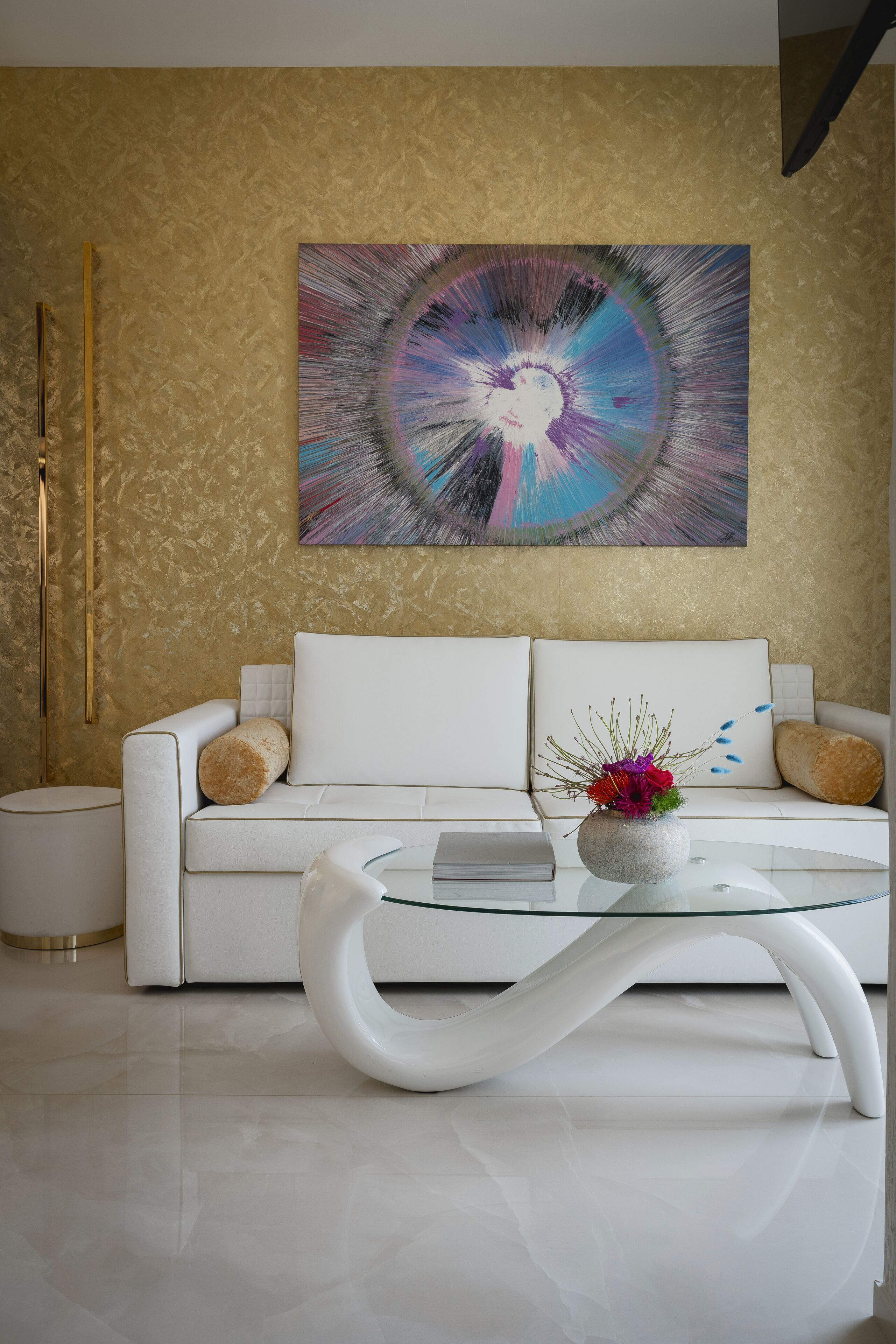 A modern living room with a white sofa, a glass coffee table, and a vibrant abstract painting on the wall.