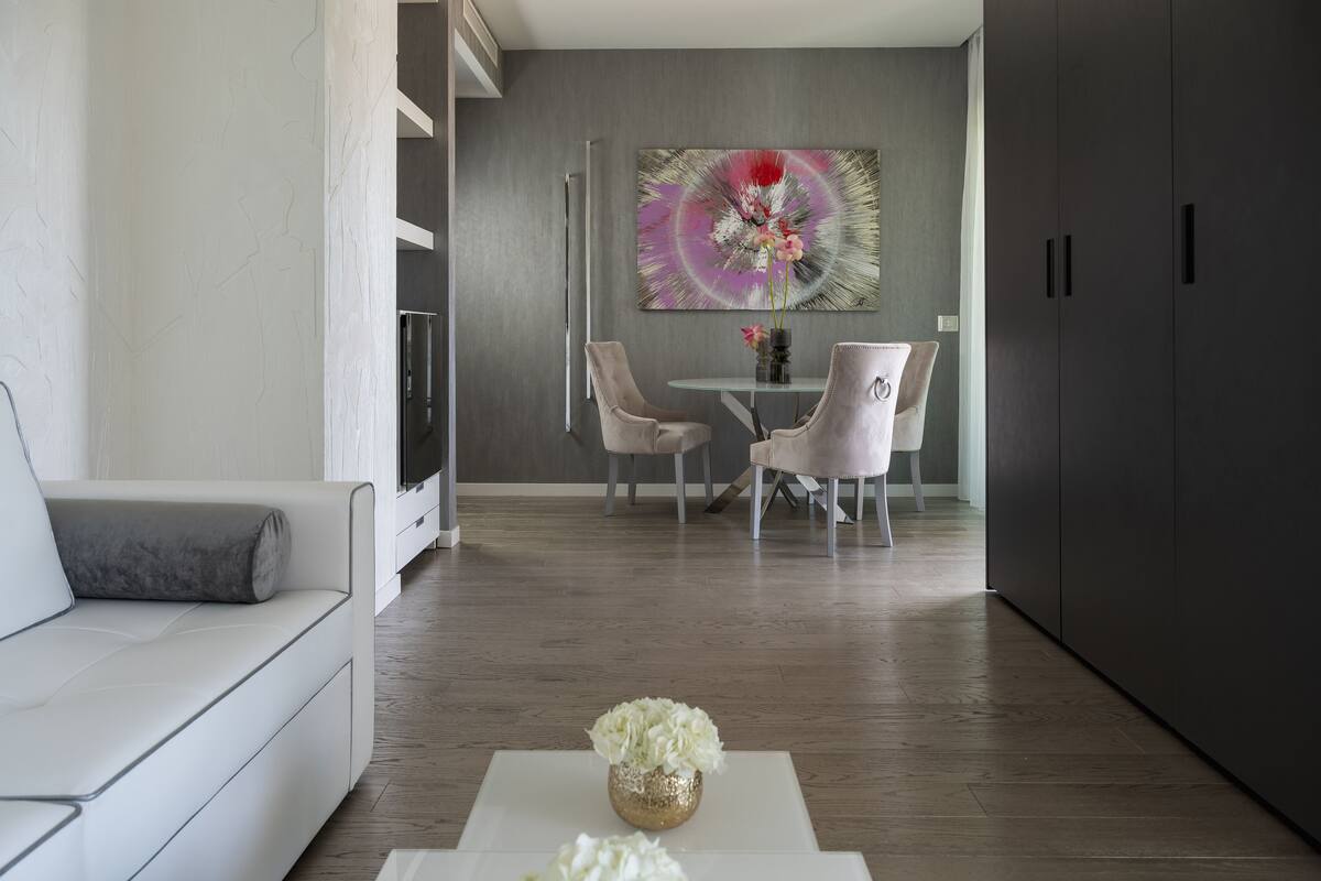 A modern living room with a sofa, a coffee table with flowers, a dining area with chairs and a table, and a large abstract painting on the wall.