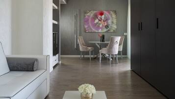 A modern living room with a sofa, a coffee table with flowers, a dining area with chairs and a table, and a large abstract painting on the wall.