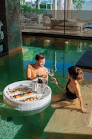 Escena junto a la piscina con una mesa de comedor, una botella de champán y una mujer y un hombre sentados.