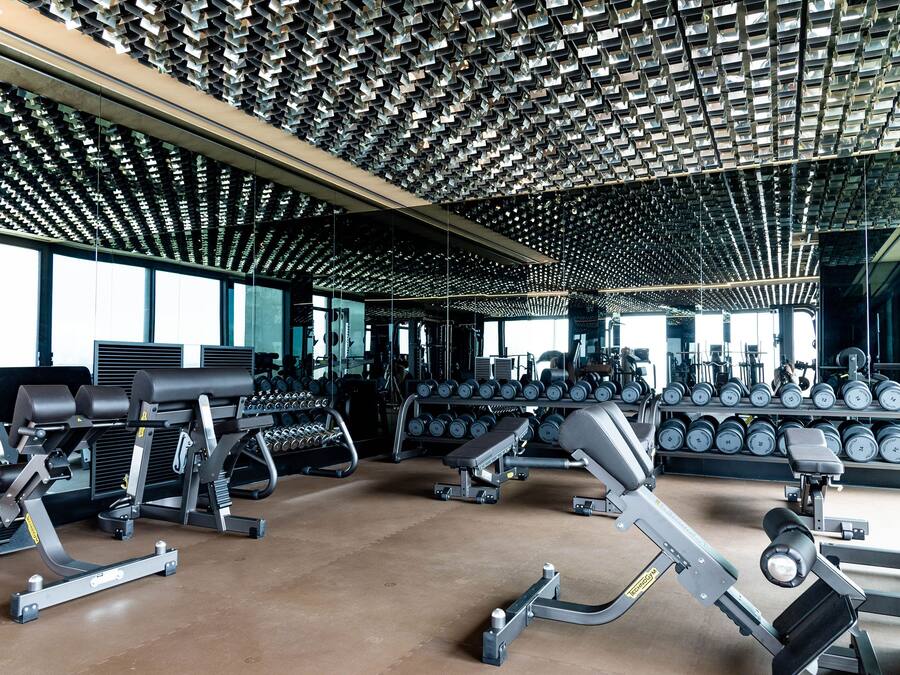 A gym with various exercise equipment, including dumbbells and weight machines, and a ceiling with a unique geometric pattern.