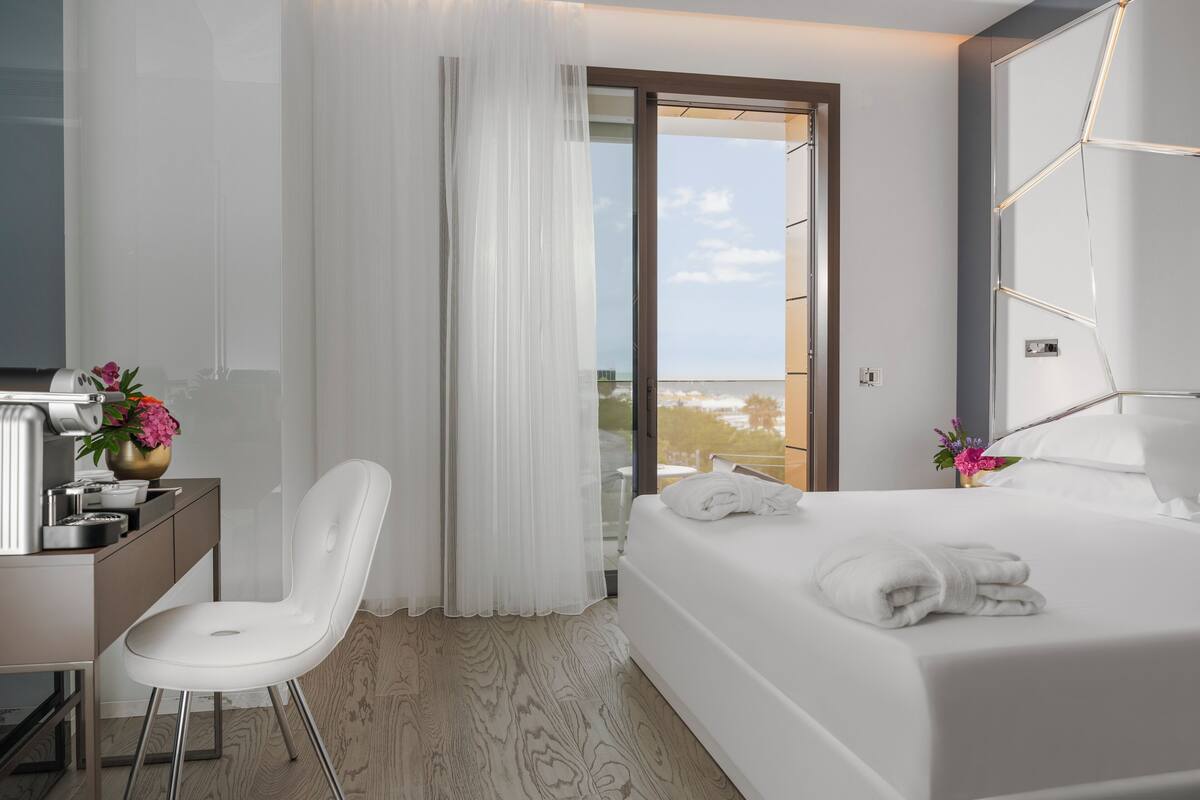 A hotel room with a bed, a desk, a chair, and a view of the outdoors.