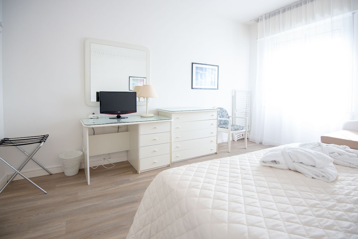 A hotel room with a bed, a desk with a computer, a chair, and a window with curtains.