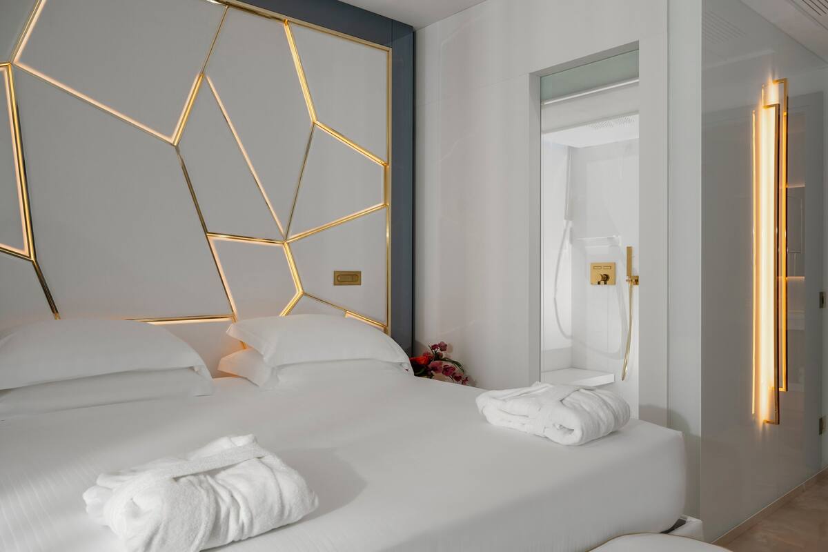 A modern hotel room with a geometric-patterned headboard, a neatly made bed with white linens, and a visible bathroom with a shower.