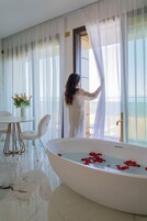 Una habitación con una bañera grande, una mesa de comedor con sillas y cortinas translúcidas.