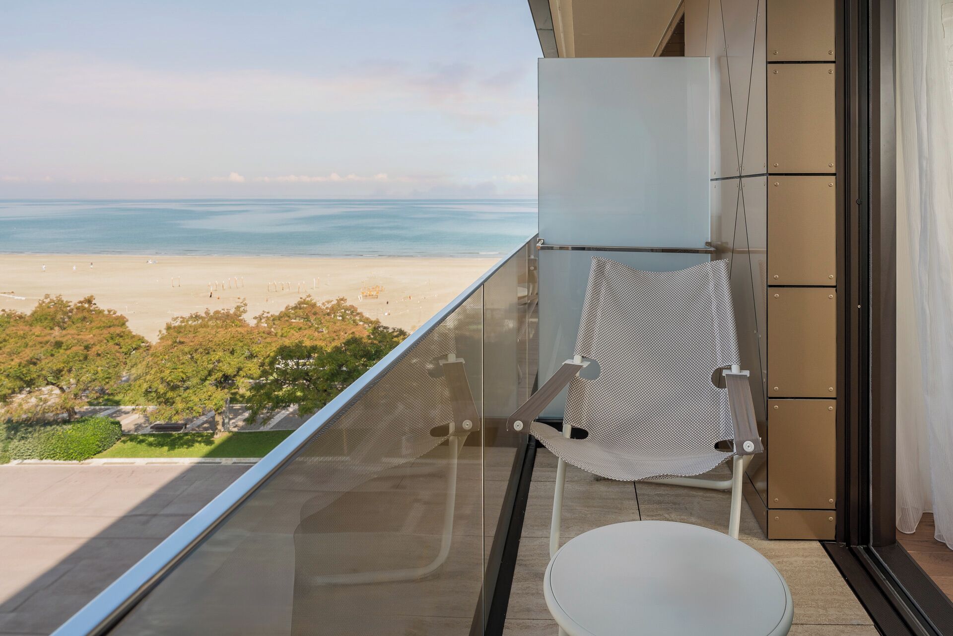 Un balcón con vistas despejadas a la playa, una silla blanca y una mesita.