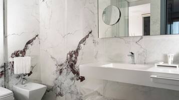 A bathroom with a marble wall, a sink, a mirror, and a toilet.