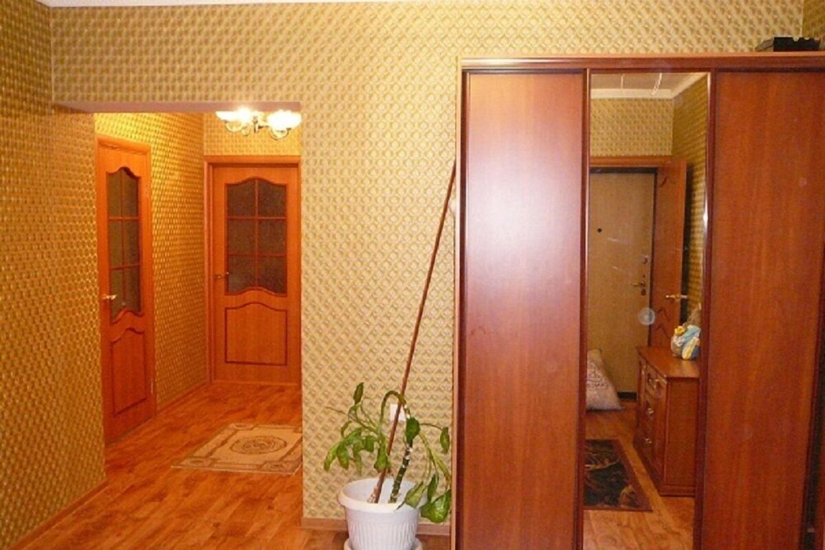 A hallway with patterned wallpaper, wooden flooring, and a potted plant.
