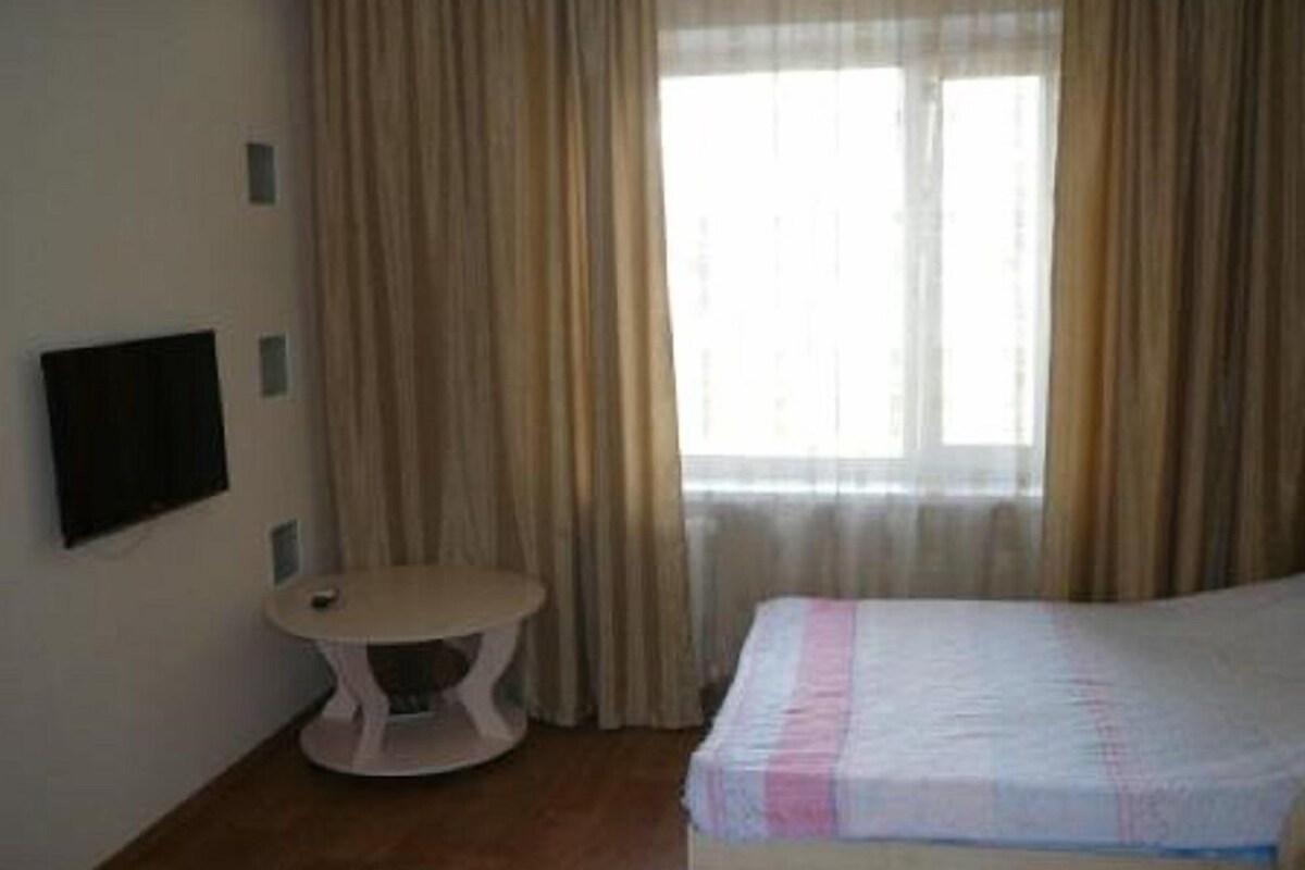 A room with a bed, a small round table, a TV mounted on the wall, and a window with curtains.