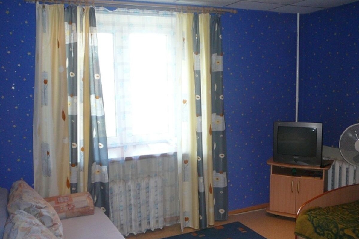 A room with a bed, a television on a stand, and a window with curtains.