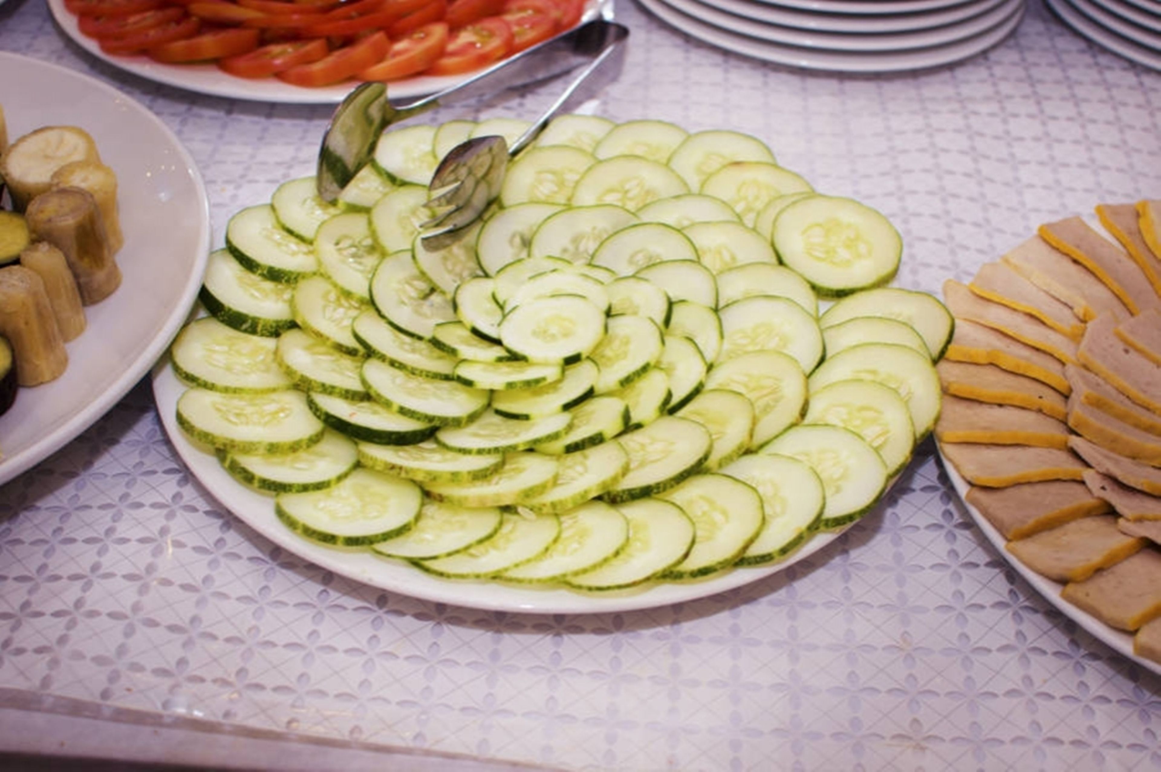 Ein Tisch mit einer Schüssel mit Gurken- und Tomatenscheiben, einer Schüssel mit Bananenscheiben und einer Schüssel mit Käsescheiben.