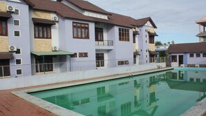 A swimming pool with a clear water surface, surrounded by multi-story buildings with balconies and air conditioning units. - Quang Nam University Guesthouse (Da Nang)