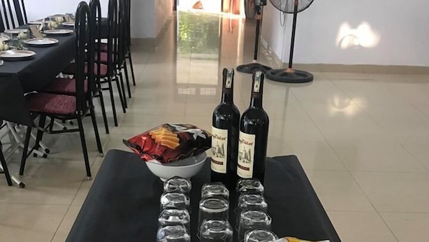 A dining table set with wine bottles, glasses, and snacks in a room with chairs and a fan. - Quang Nam University Guesthouse (Da Nang)