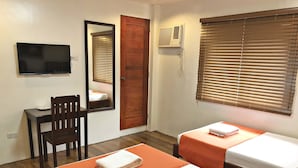 A hotel room with two beds, a desk, a chair, a TV, a door, and a window with blinds. - Casa Roces Bed and Breakfast (Legazpi)