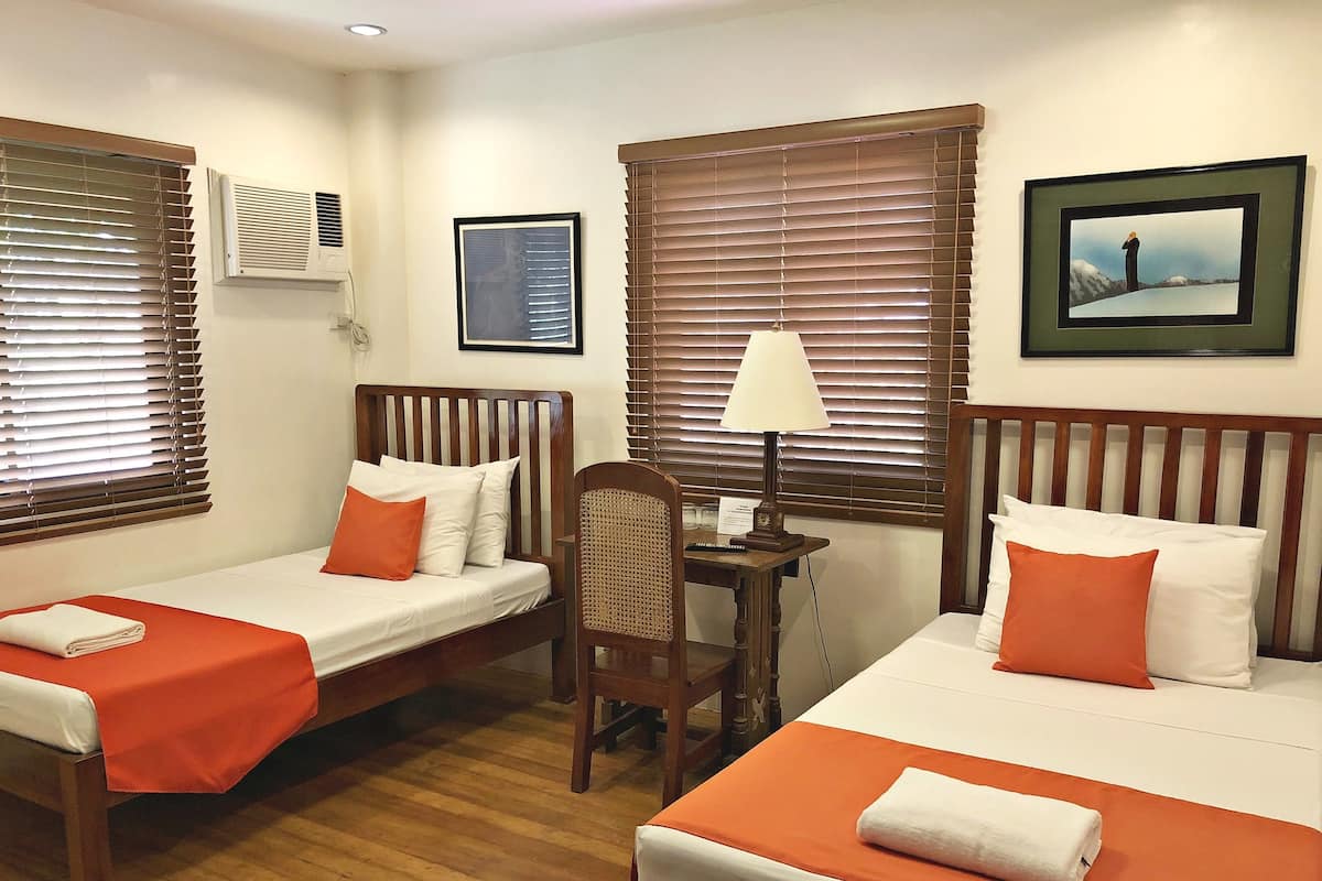 A hotel room with two single beds, a wooden desk, and a chair.