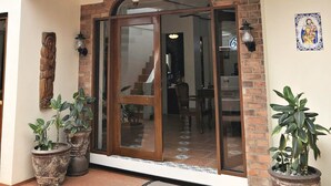 A covered entrance with a glass door, potted plants, and a brick wall. - Casa Roces Bed and Breakfast (Legazpi)