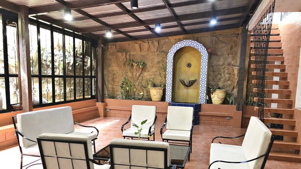 A sunlit patio with white cushioned chairs, a glass table, and a decorative fountain. - Casa Roces Bed and Breakfast (Legazpi)