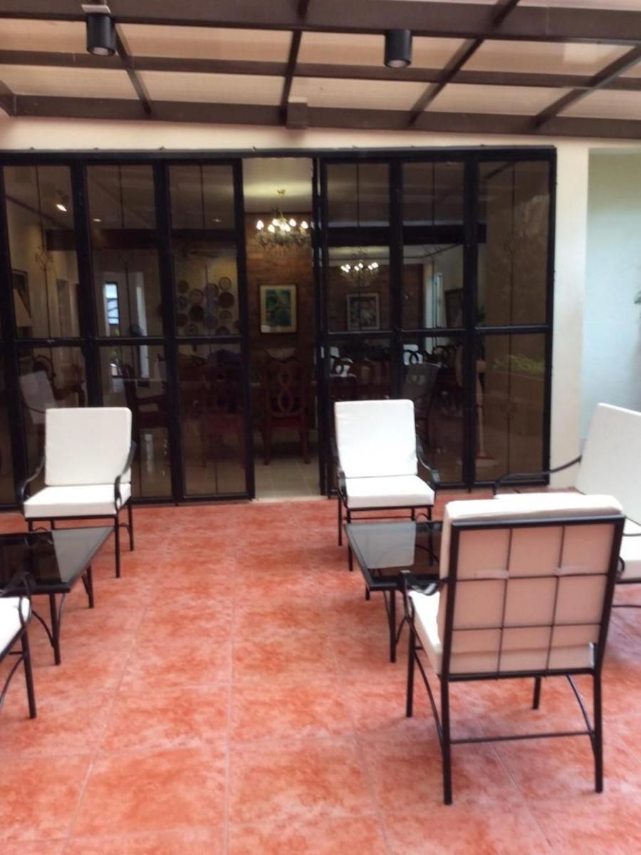 Una habitación con puerta de vidrio que da a un comedor, con dos sillas blancas acolchadas y una mesa.