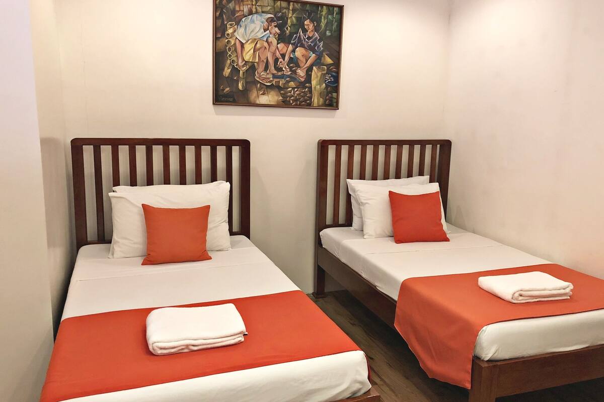 Two single beds with wooden headboards, white bedding, and orange accents.