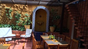An outdoor patio with wooden furniture, a patterned wall, and potted plants. - Casa Roces Bed and Breakfast (Legazpi)