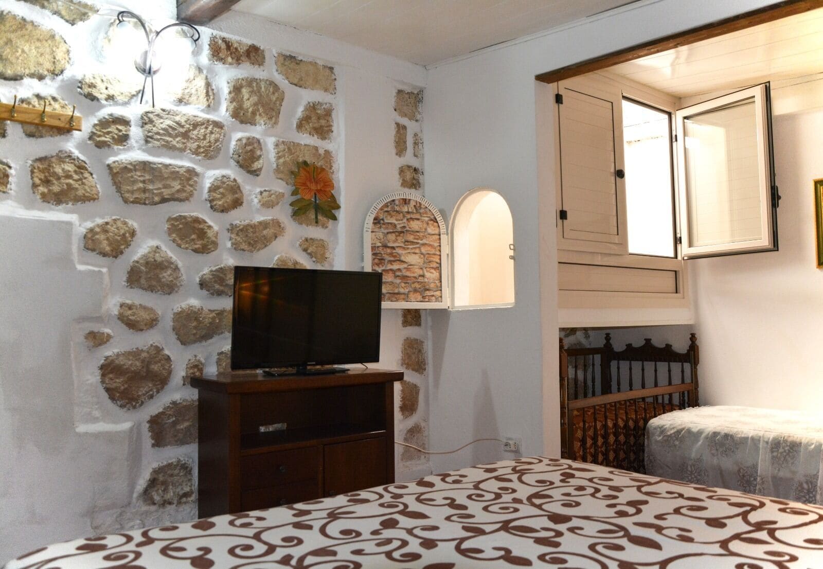A bedroom with a stone wall, a television on a wooden stand, a bed with patterned bedding, and a wooden headboard.