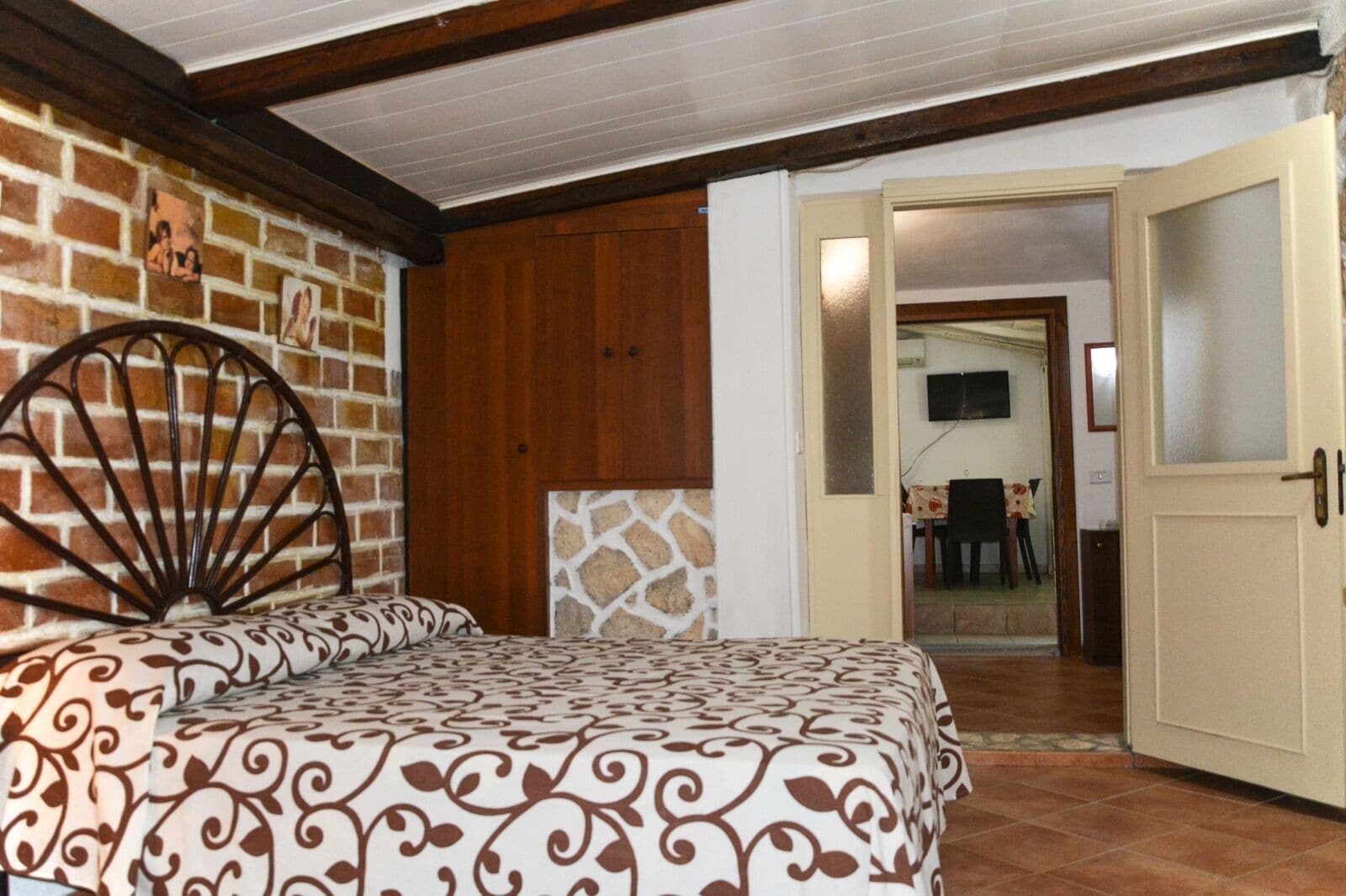 Un dormitorio con cama, pared de ladrillo, paneles de madera y una puerta que da a otra habitación.