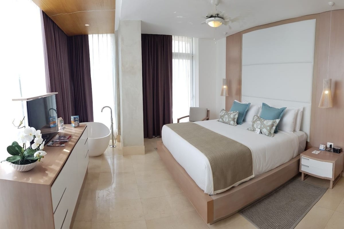 Une chambre d’hôtel moderne avec un grand lit, un bureau équipé d’un ordinateur, un lavabo et une plante en pot.