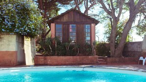 A pool area with a wooden structure, possibly a pool house, surrounded by trees and a concrete wall.