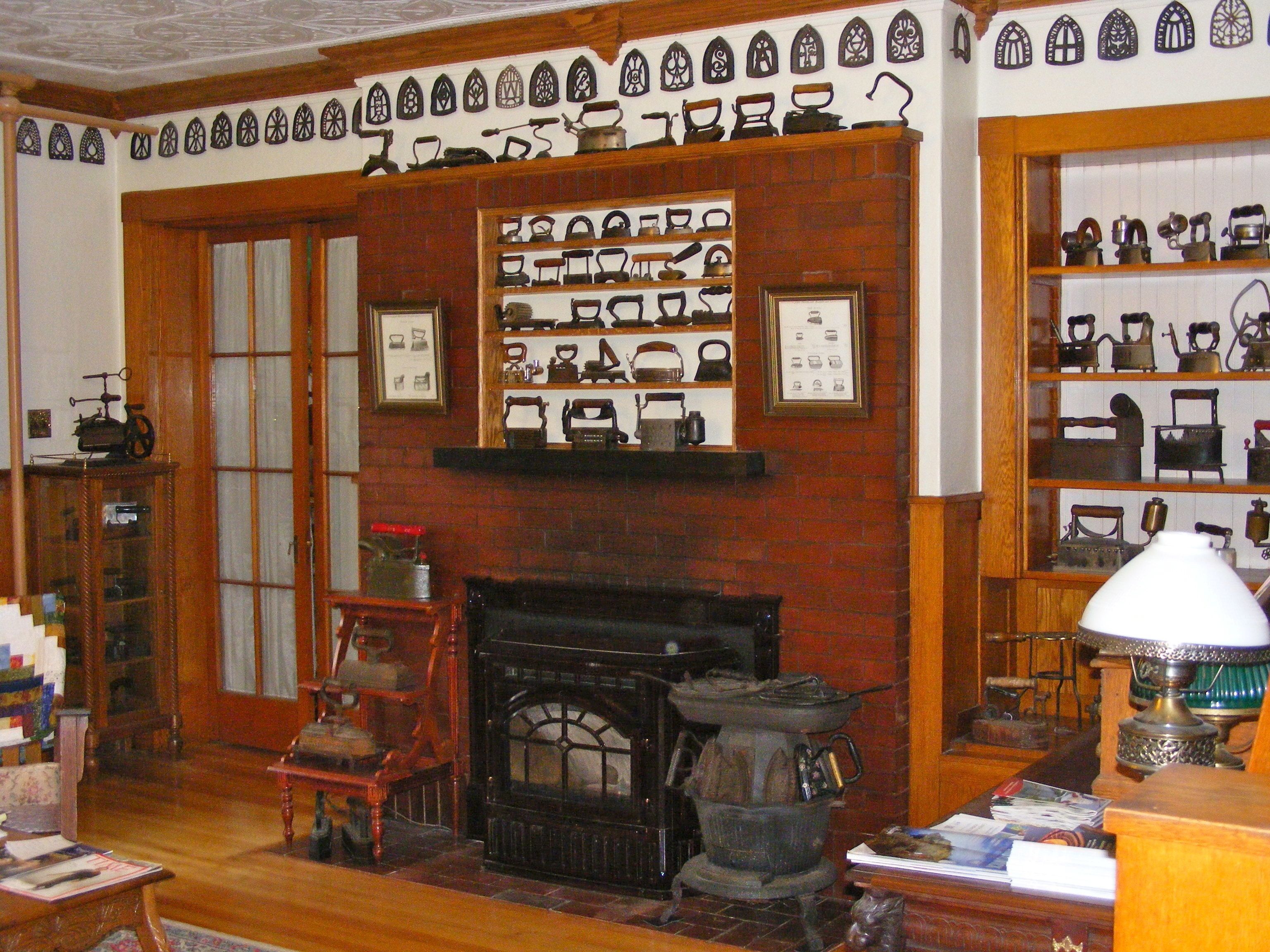 Una habitación con chimenea, estanterías de madera con utensilios de cocina y una exhibición de utensilios de cocina antiguos.