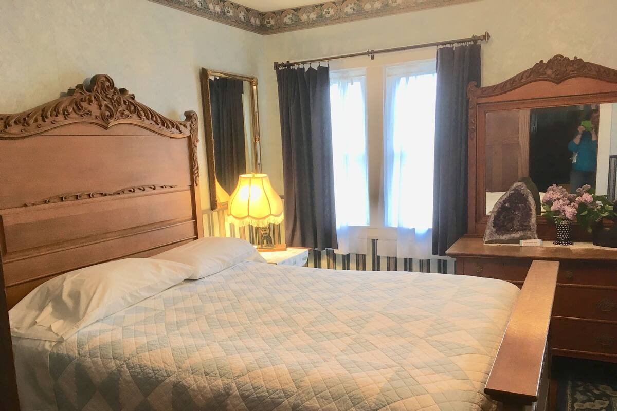 Una camera da letto con un letto grande, una testiera in legno, un comodino con una lampada, un comò e uno specchio.