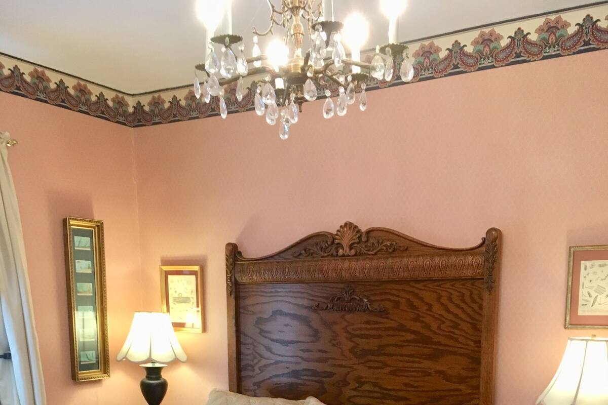 Un letto rifatto con cura, con una testiera in legno, due lampade ai comodini e un lampadario sopra.