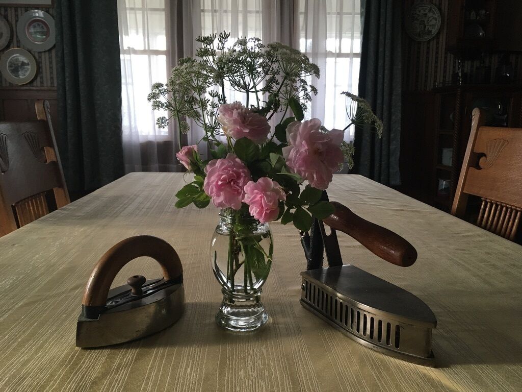 Una mesa de madera con un jarrón de flores rosas, un planchador de hierro antiguo y un planchador moderno.