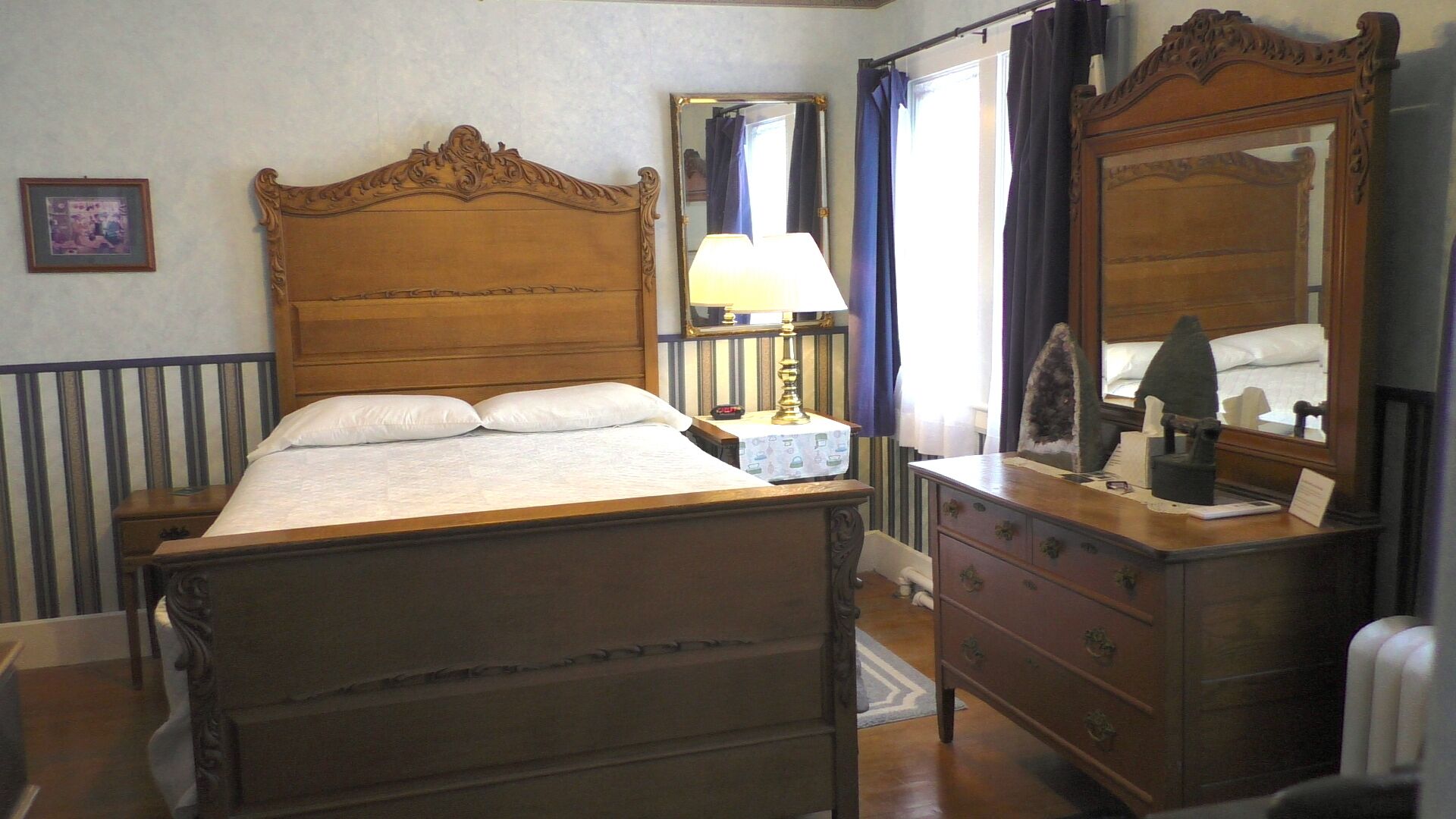 A wooden bed with a headboard, a bedside table with a lamp, a dresser with drawers, and a mirror.