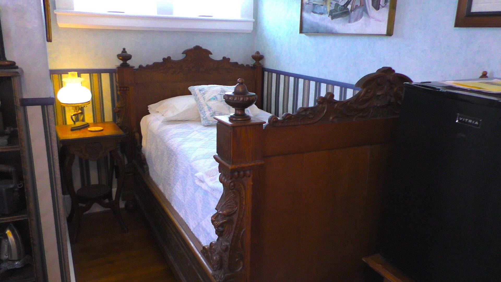 A narrow room with a wooden bed, a bedside table with a lamp, and a television.