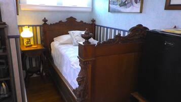 A narrow room with a wooden bed, a bedside table with a lamp, and a television.