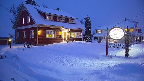A snow-covered building with a sign indicating weekly/monthly rentals. - Old Iron Inn Bed and Breakfast (Caribou)