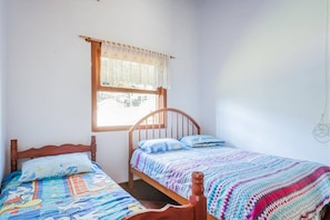 A bedroom with a wooden bed, a window with a lace curtain, and a wall-mounted light fixture.