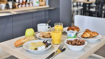 Una mesa de desayuno con platos de comida, incluyendo croissants, un tazón de cereal y un vaso de jugo de naranja.