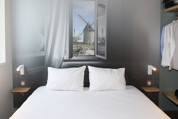 Une chambre à coucher avec un grand lit, deux tables de chevet, une fenêtre donnant sur un moulin et un rideau.