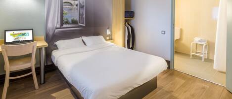 Habitación de hotel con cama, escritorio con una computadora portátil, ventana con vista a un puente y baño con cortina de ducha.