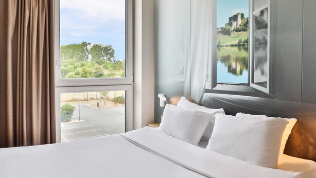 A hotel room with a large bed, a view of a lake, and a painting of a castle. - B&B HOTEL LES HERBIERS (Les Herbiers)