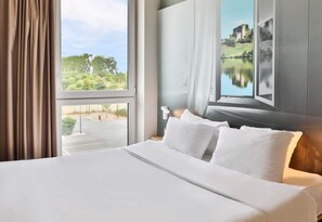 Une chambre d  ’hôtel avec un grand lit, une vue sur un lac et un tableau représentant un château.
