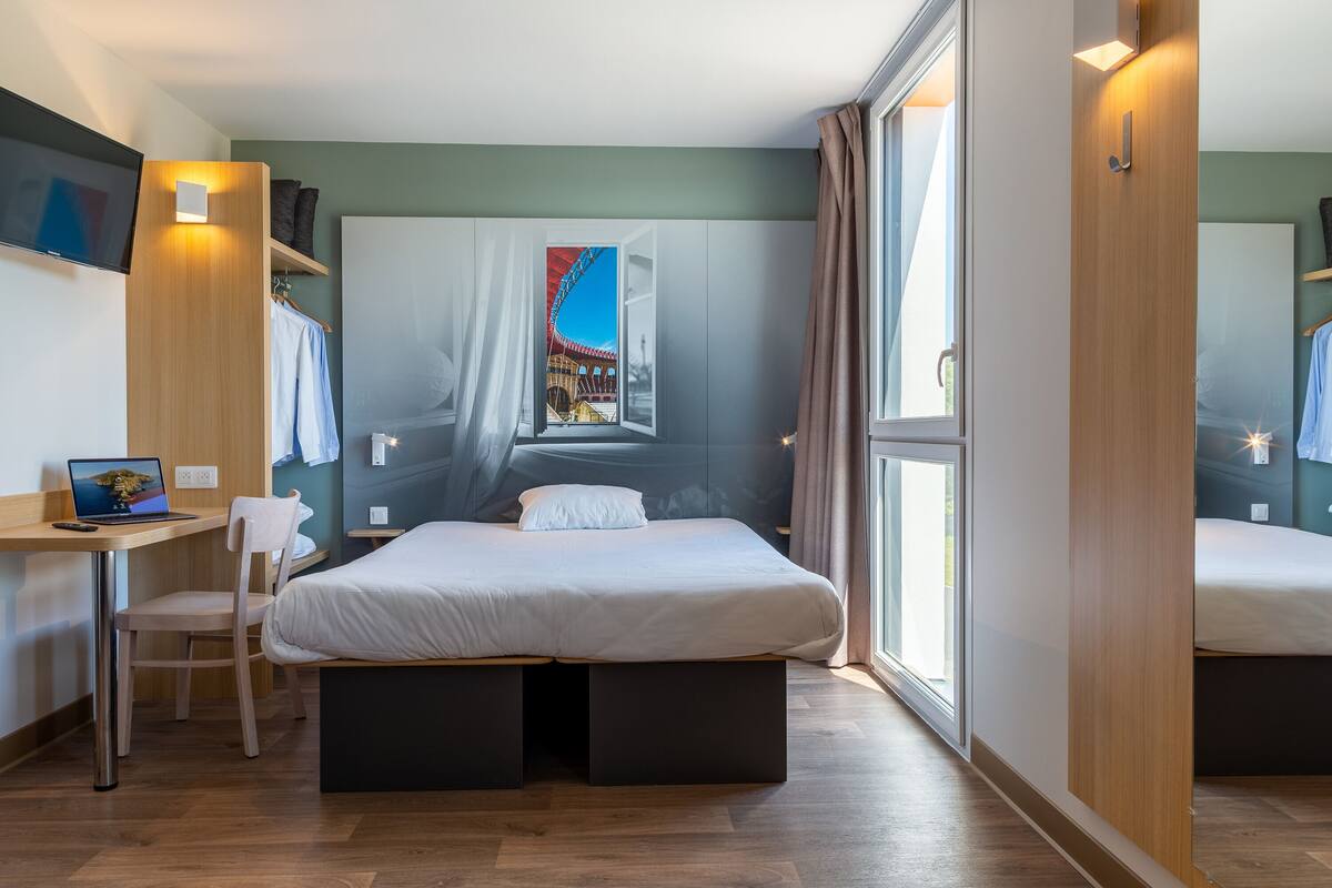 A modern hotel room with a bed, a desk, and a laptop.