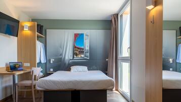A modern hotel room with a bed, a desk, and a laptop.