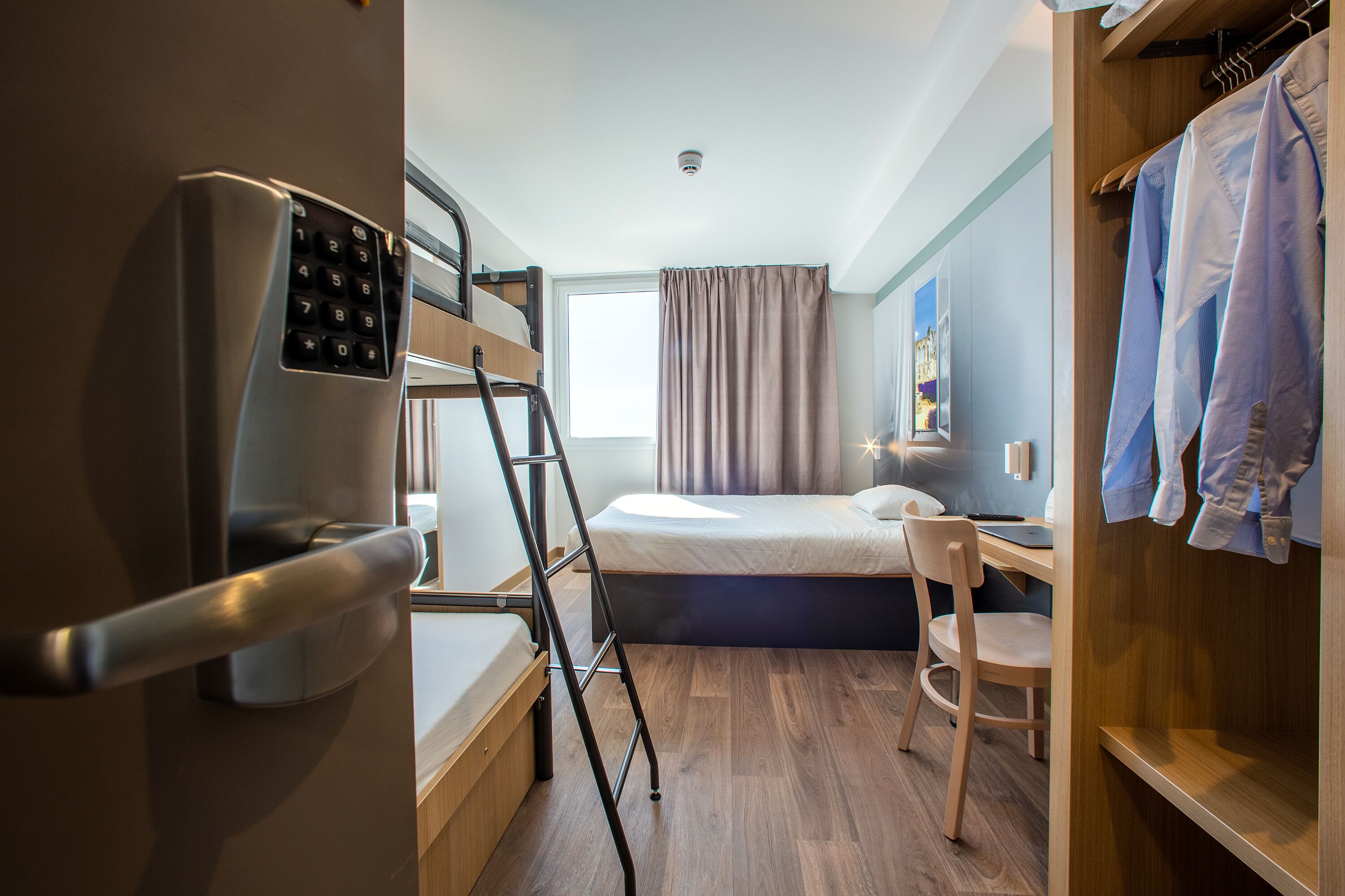 Una habitación de hotel pequeña con una cama litera, un escritorio y un armario.