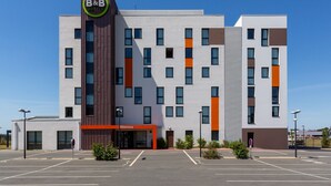 A modern B&B hotel with a central entrance, multiple floors, and a parking lot. - B&B HOTEL LES HERBIERS (Les Herbiers)