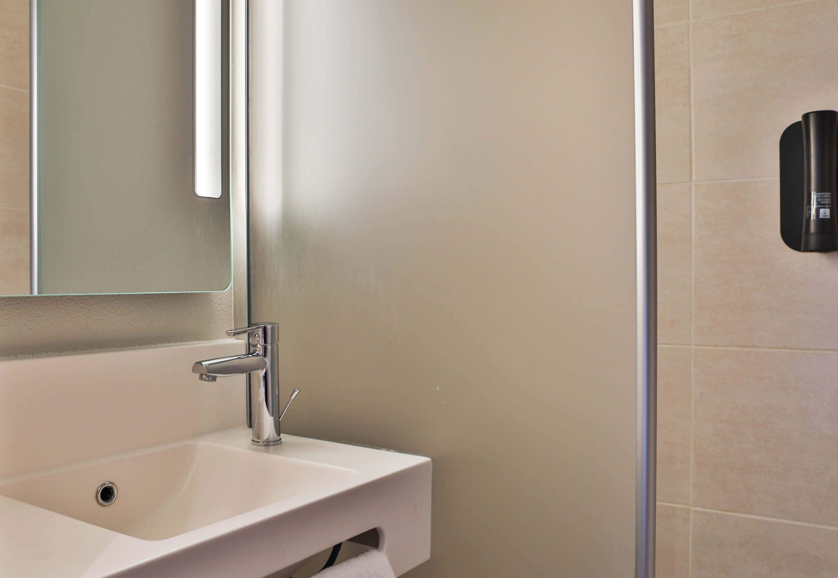 Un baño con un lavamanos blanco, un espejo y un dispensador de jabón en la pared.