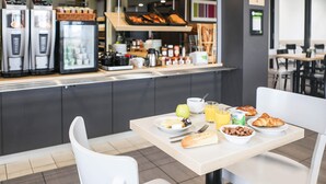 A breakfast setup with a table, chairs, and a counter with food items and beverages. - B&B HOTEL LES HERBIERS (Les Herbiers)