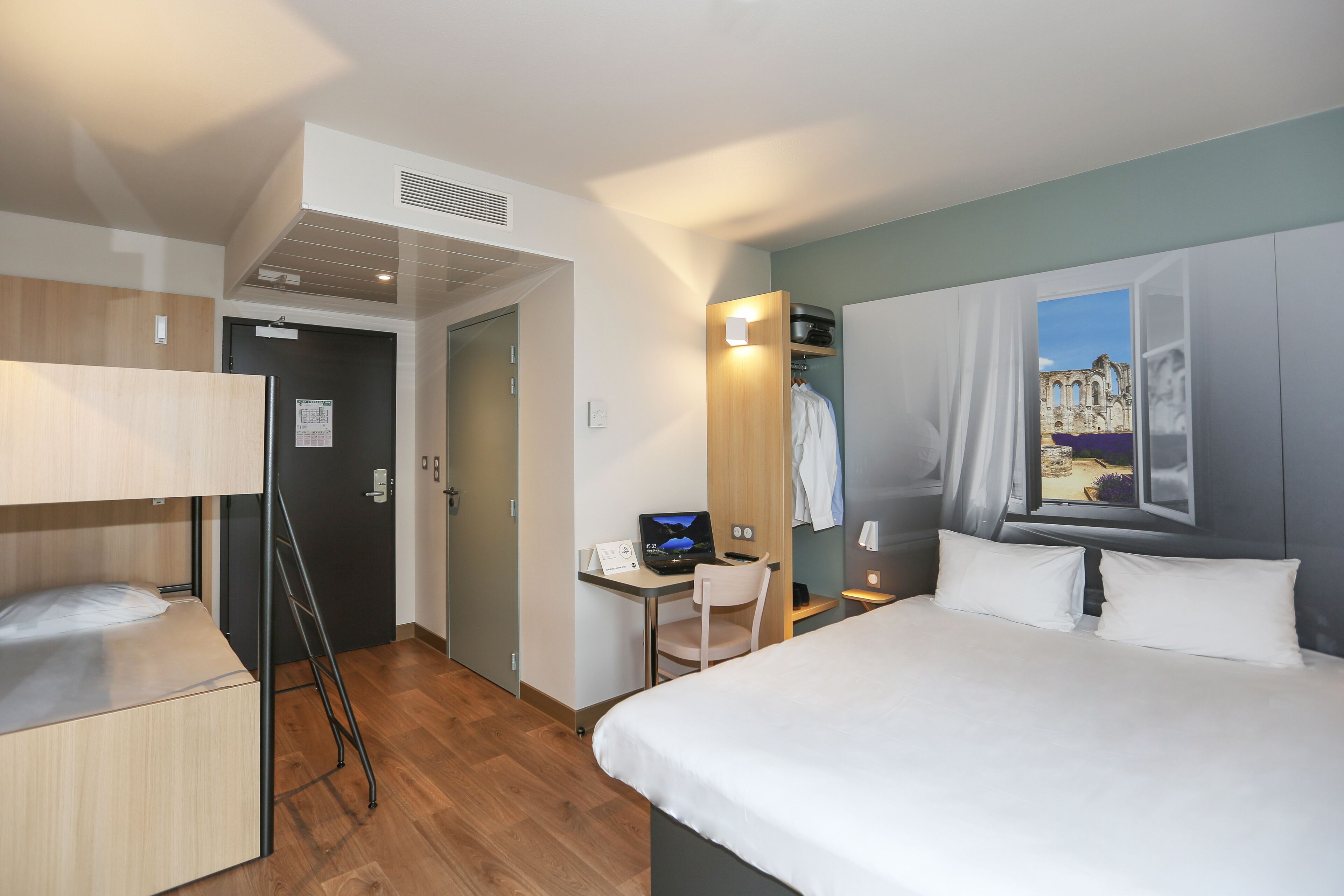 Ett hotellrum med en säng, ett skrivbord med en bärbar dator, en stol och en garderob.