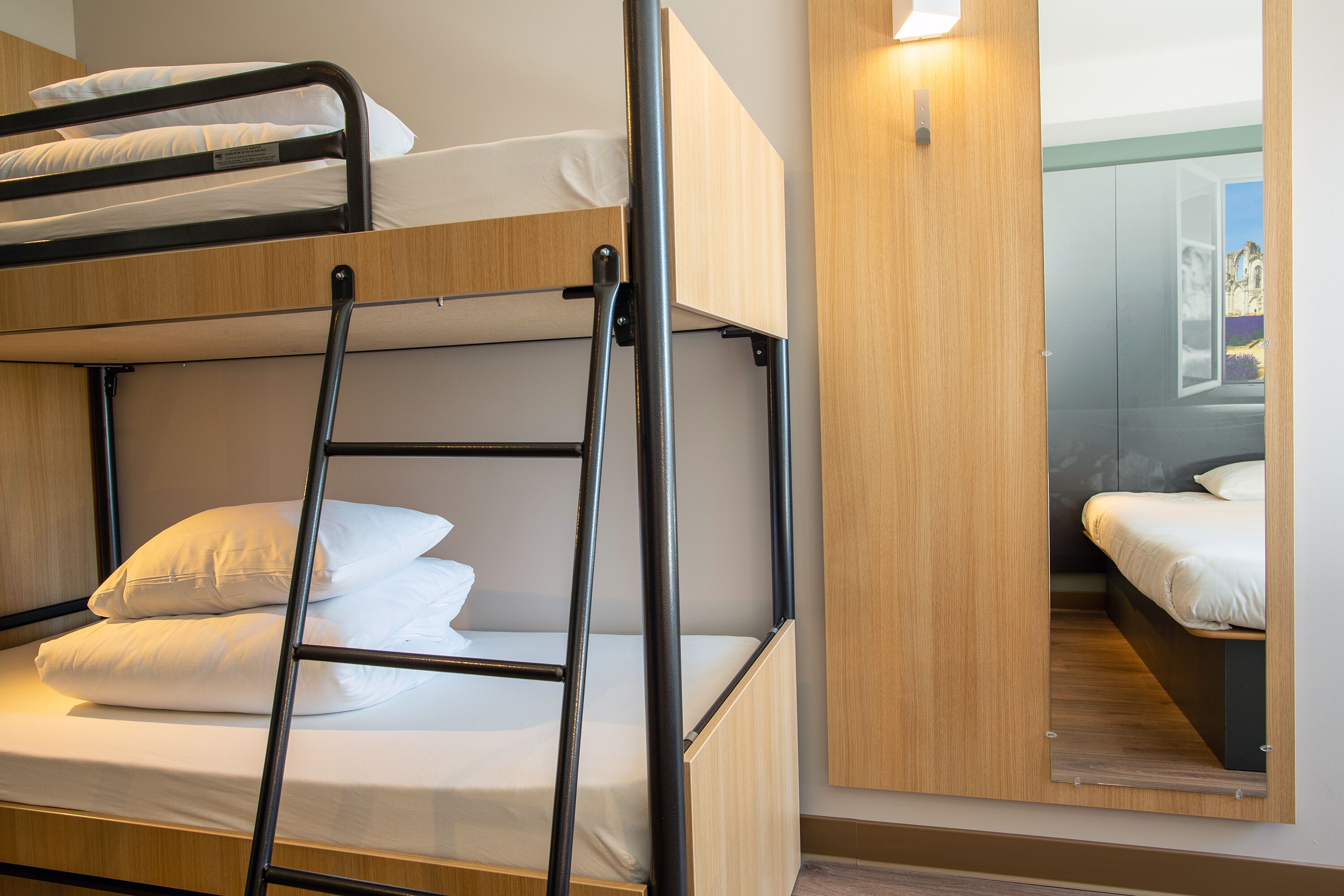 Une chambre avec un lit superposé, une échelle, une tête de lit en bois et un miroir au mur.